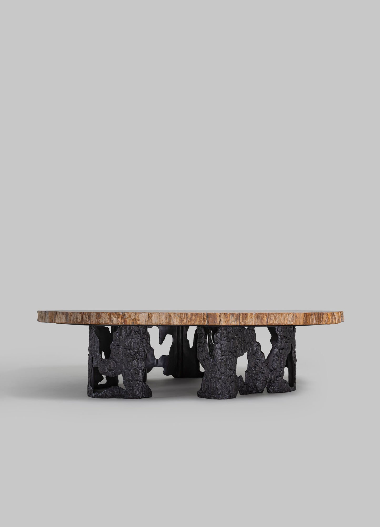 A coffee table with a circular wooden top and a black base made of textured, irregularly shaped material resembling charred or burnished wood, showcasing a rustic and contemporary style.