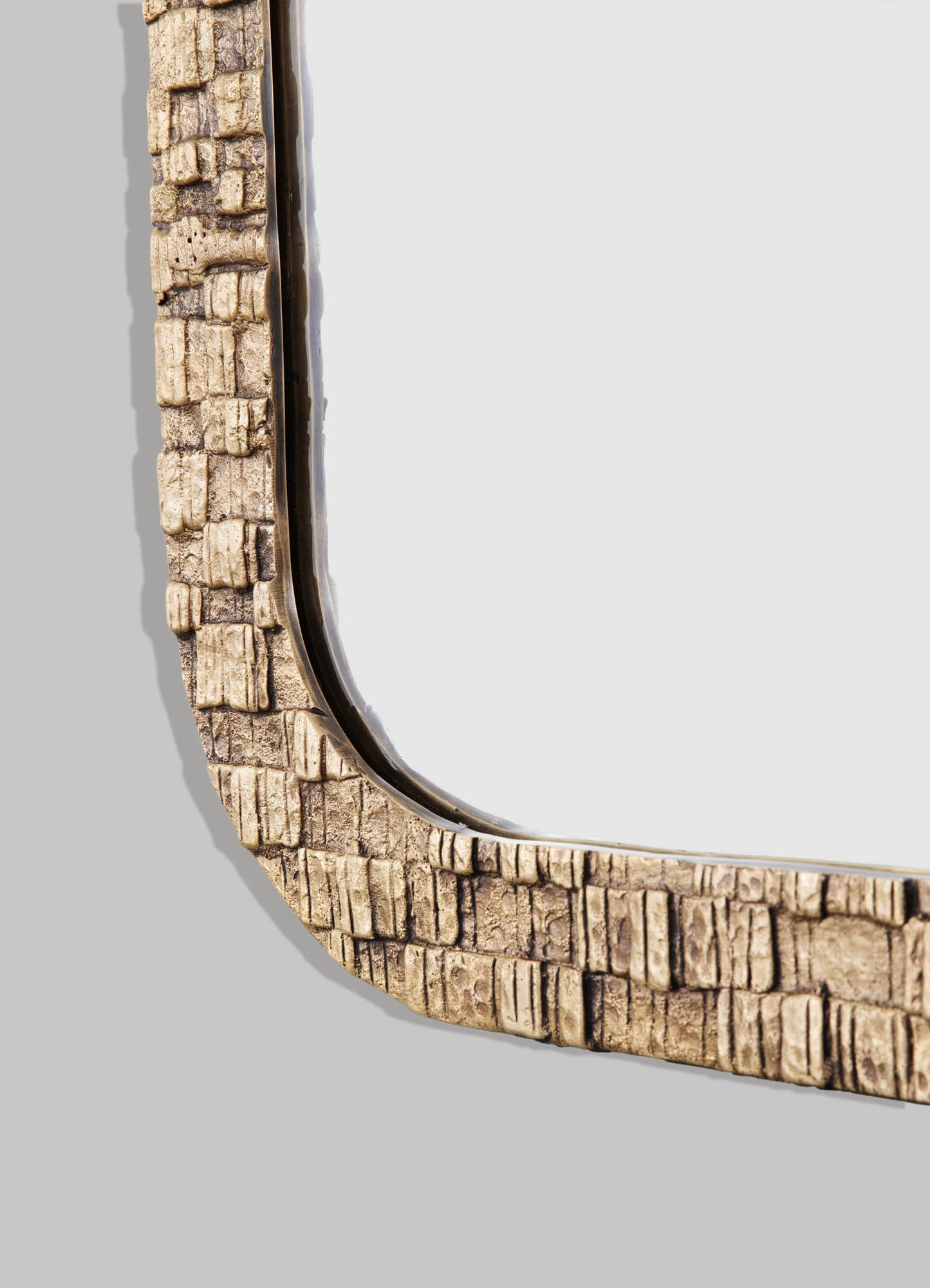 A close-up of a mirror with a textured, rustic frame made of beige, distressed wood and a brass inner edge. The overall style is rustic and handcrafted, highlighting natural materials and organic motifs.