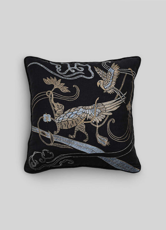 The Viya Dreamscape Leophant Black & Gold Embroidered Linen Cushion Cover (24"x24") showcases a mythical winged creature, bird, and swirling motifs in gold and silver embroidery on a square black design.