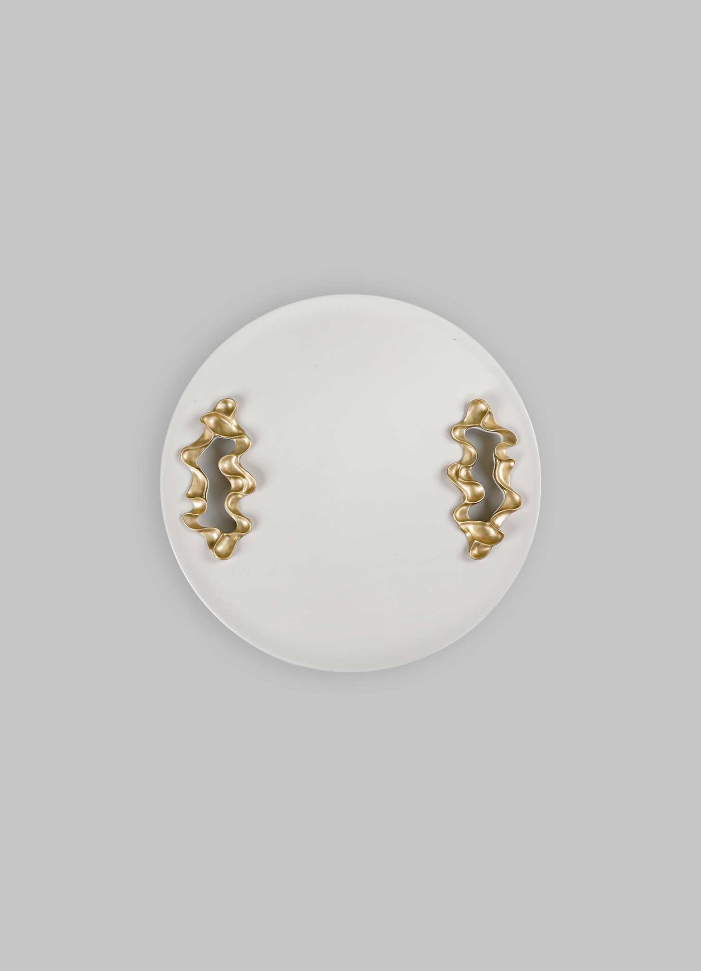 Ceramic wall plate with beige matte finish, featuring two abstract, irregularly shaped metallic gold handles with a wavy design, set against a light gray background.