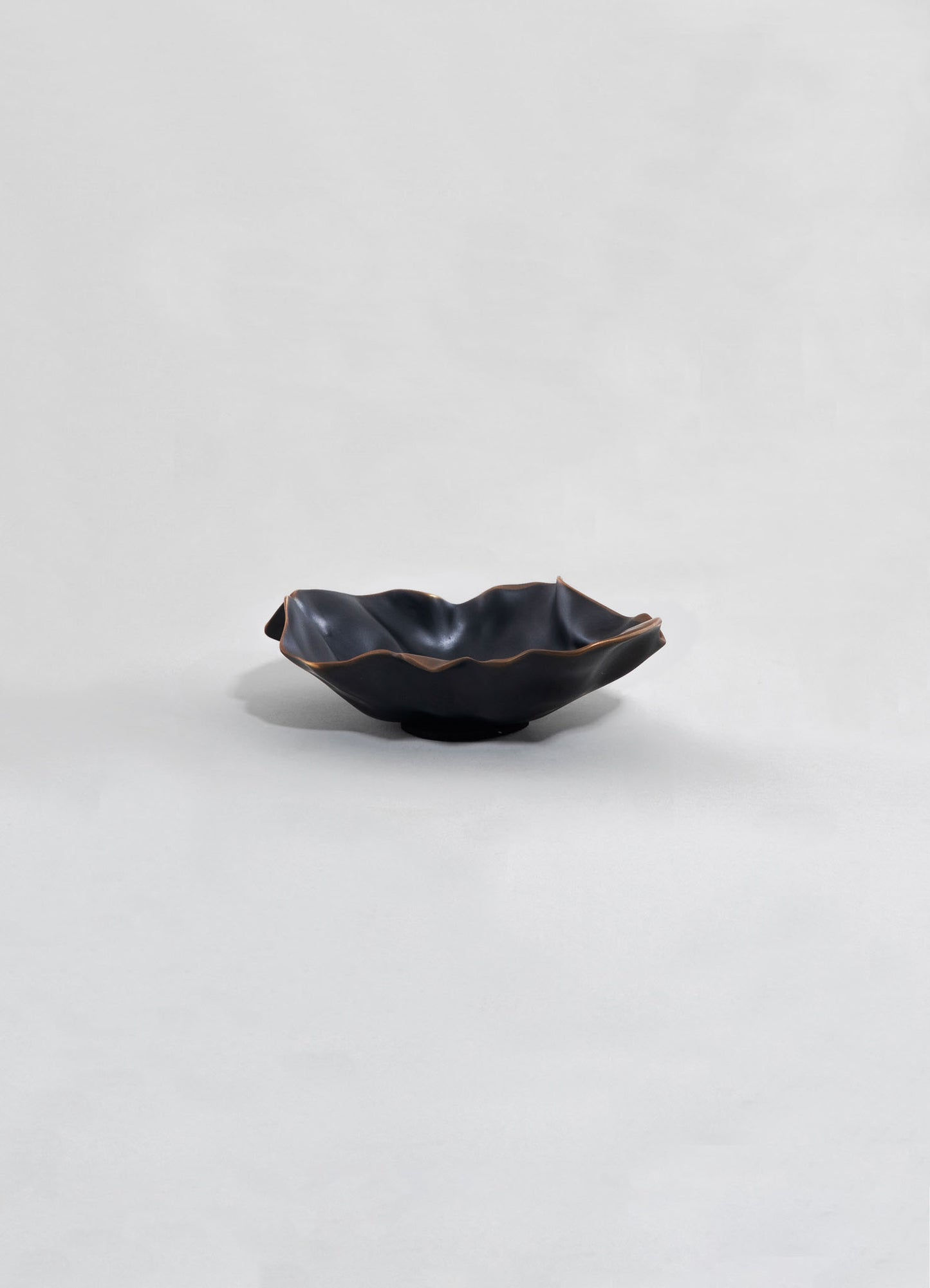 Black ceramic bowl with an irregular, ruffled edge and a matte finish, set against a plain light background.