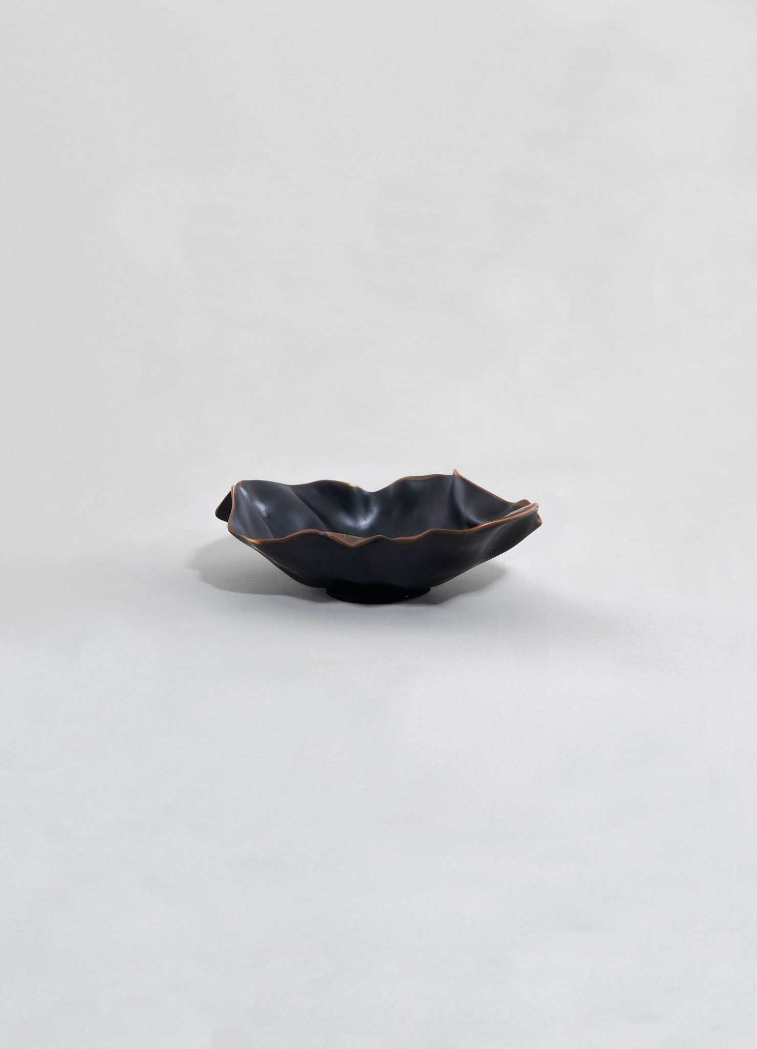 Black ceramic bowl with an irregular, ruffled edge and a matte finish, set against a plain light background.