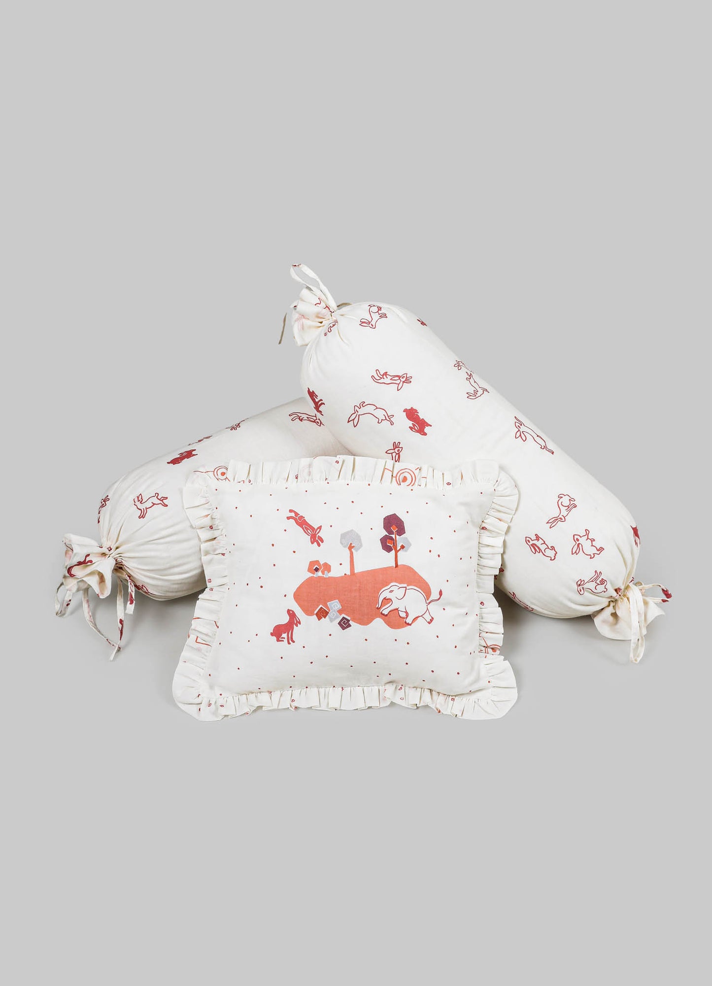 Children's bedding set comprising a ruffled pillow with an illustrated landscape, a long bolster pillow with tied ends, and a square cushion, all made of soft cotton fabric with whimsical animal and nature motifs in shades of red and pink.