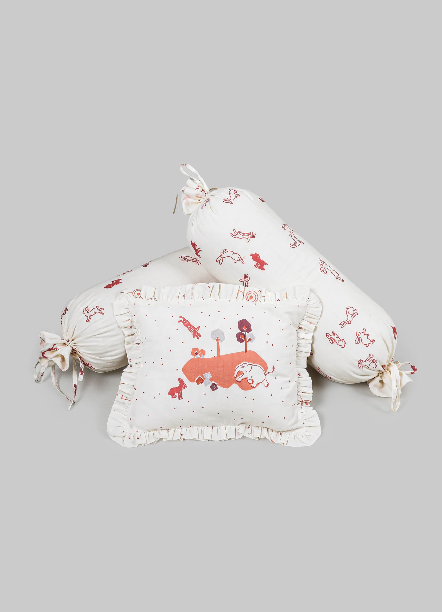 Children's bedding set comprising a ruffled pillow with an illustrated landscape, a long bolster pillow with tied ends, and a square cushion, all made of soft cotton fabric with whimsical animal and nature motifs in shades of red and pink.