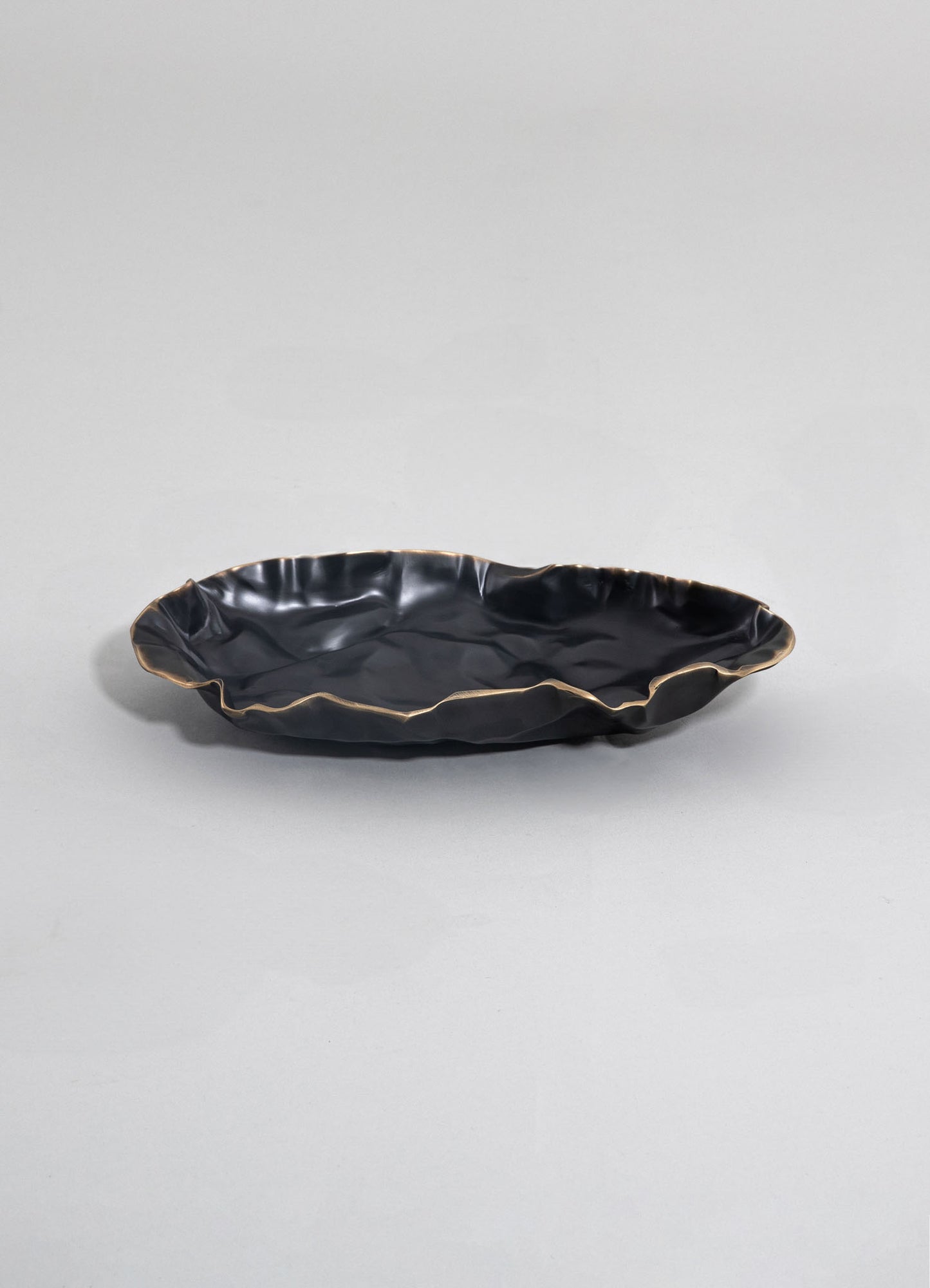 A black ceramic serving dish with a crinkled, irregular rim accented with a metallic gold finish, displayed on a plain light-colored background.