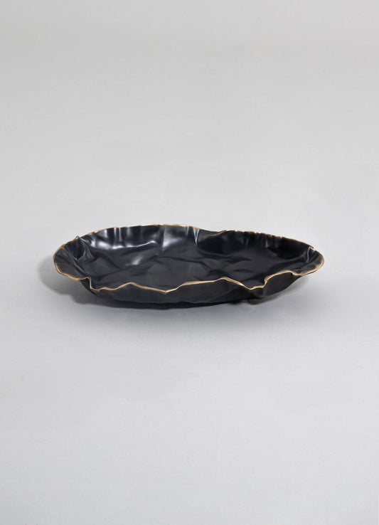 A black ceramic serving dish with a crinkled, irregular rim accented with a metallic gold finish, displayed on a plain light-colored background.