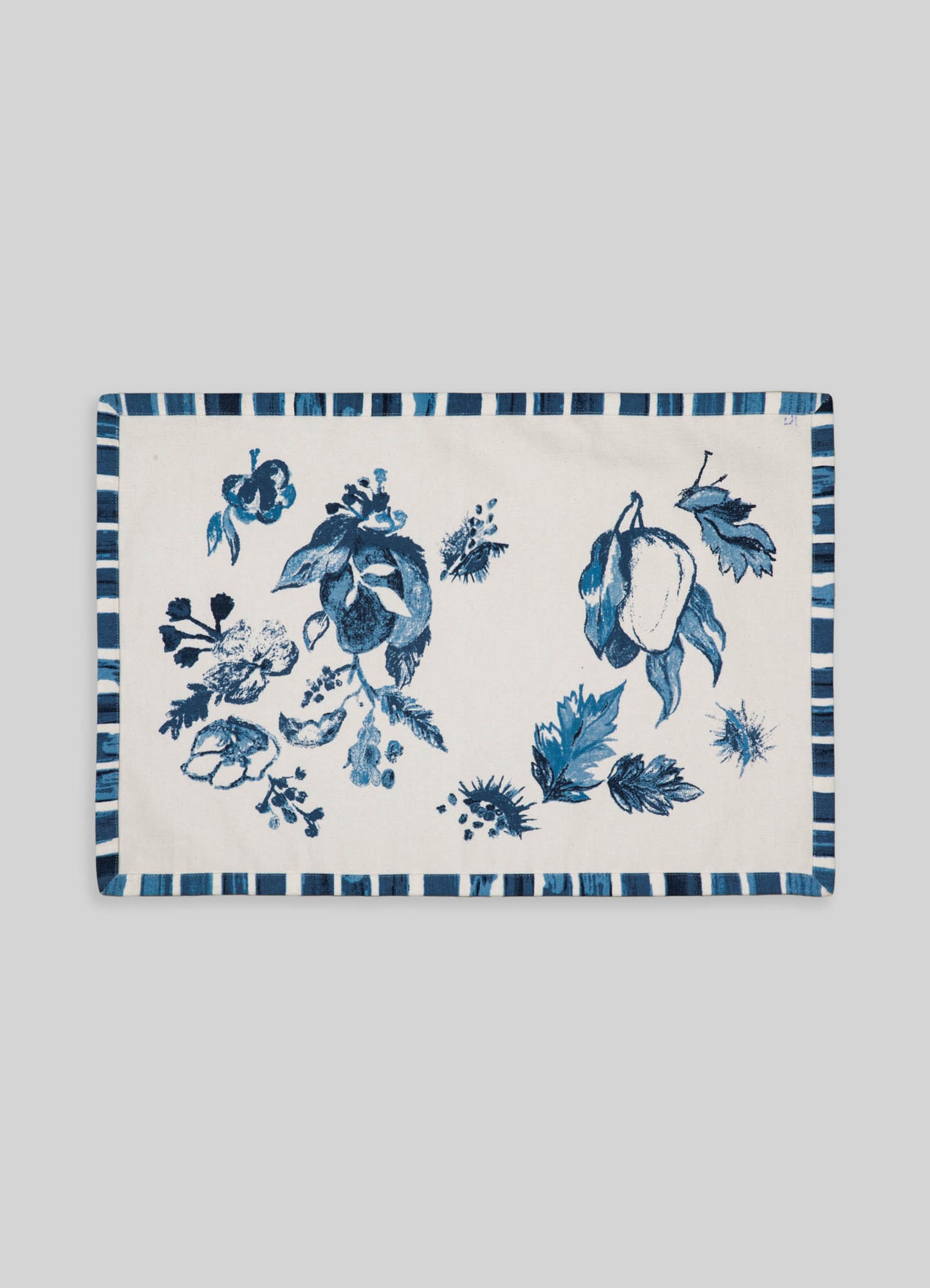 A rectangular table runner made of fabric with a white background and blue floral pattern featuring fruit and leaves, bordered by a striped blue and white design.