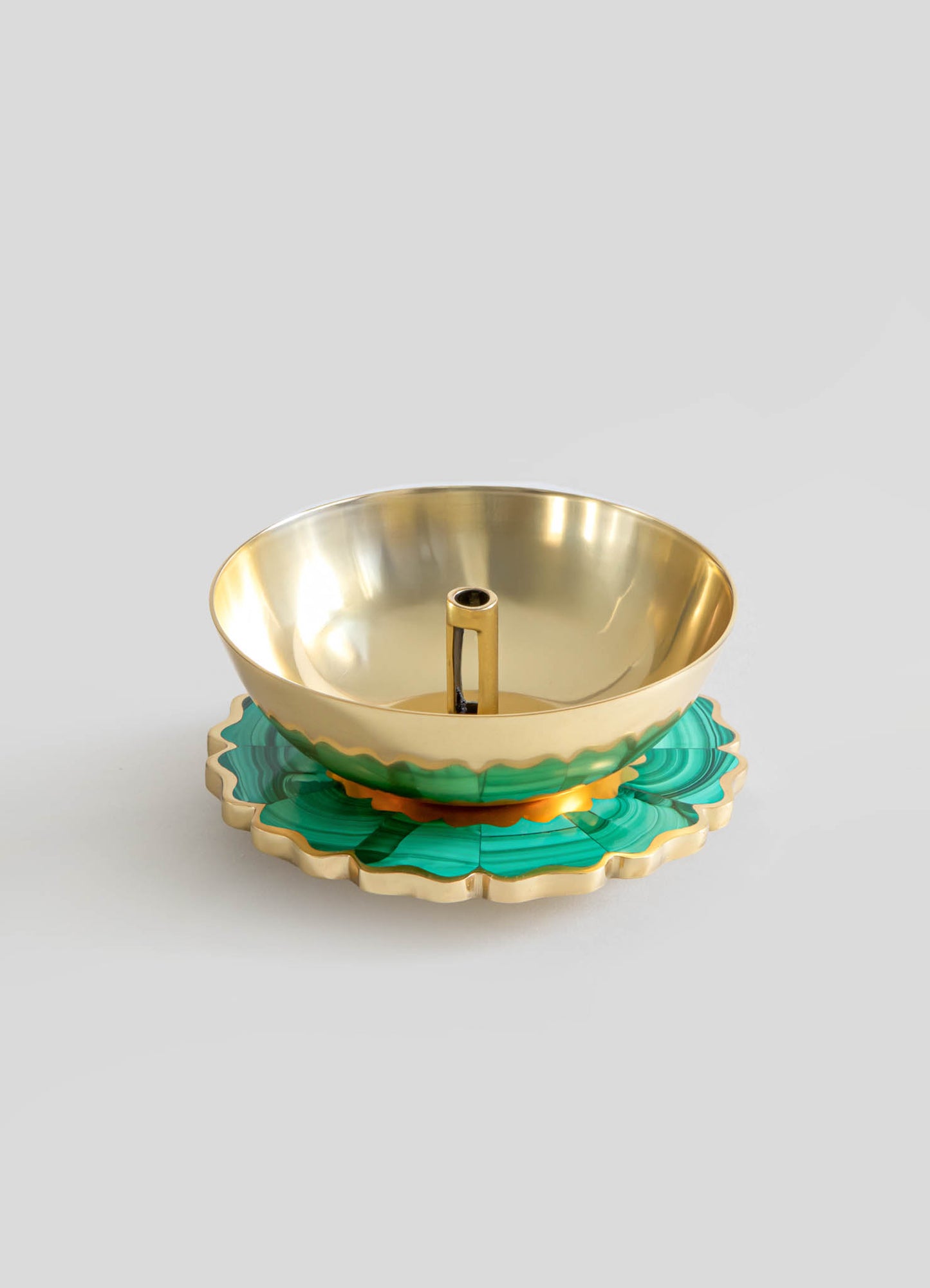 A decorative brass candle holder with a polished gold finish, featuring a circular basin with a central holder for a candle, mounted on an ornate, scalloped edge malachite-patterned base.