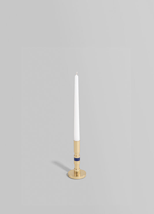 Brass candlestick holder with a round base and a vertical striped pattern in navy and natural finishes, holding a tall white taper candle.