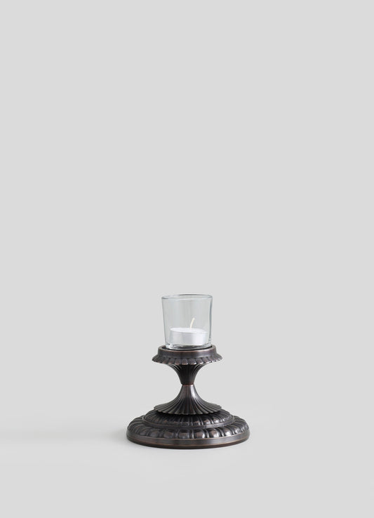 A decorative candle holder with a dark metallic finish, featuring a fluted design and a round base, topped with a glass cover that encloses a white candle.