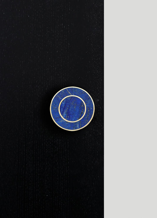 A round jewelry or accessory dish with a blue marble-like pattern and gold-colored borders, placed on a black wooden surface. The design appears contemporary and elegant, emphasizing bold color contrast and metallic accents.