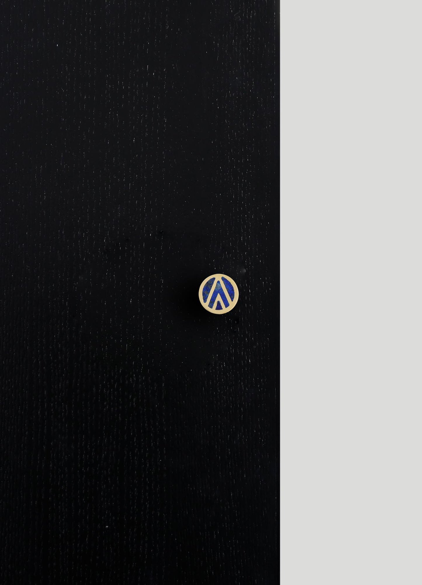 A close-up of a black fabric with a subtle textured pattern and a small circular button featuring a blue and beige geometric design. The fabric appears to have a matte finish with fine, evenly spaced stitching or weave visible.