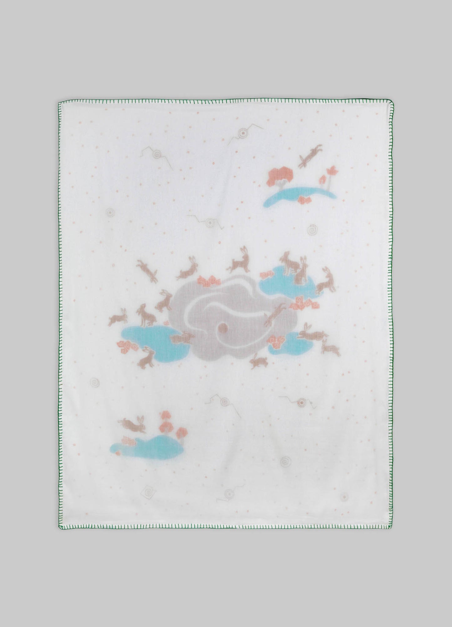 Baby burp cloth made of soft white fabric with printed pastel illustrations of rabbits, clouds, and flying birds, edged with green stitching.