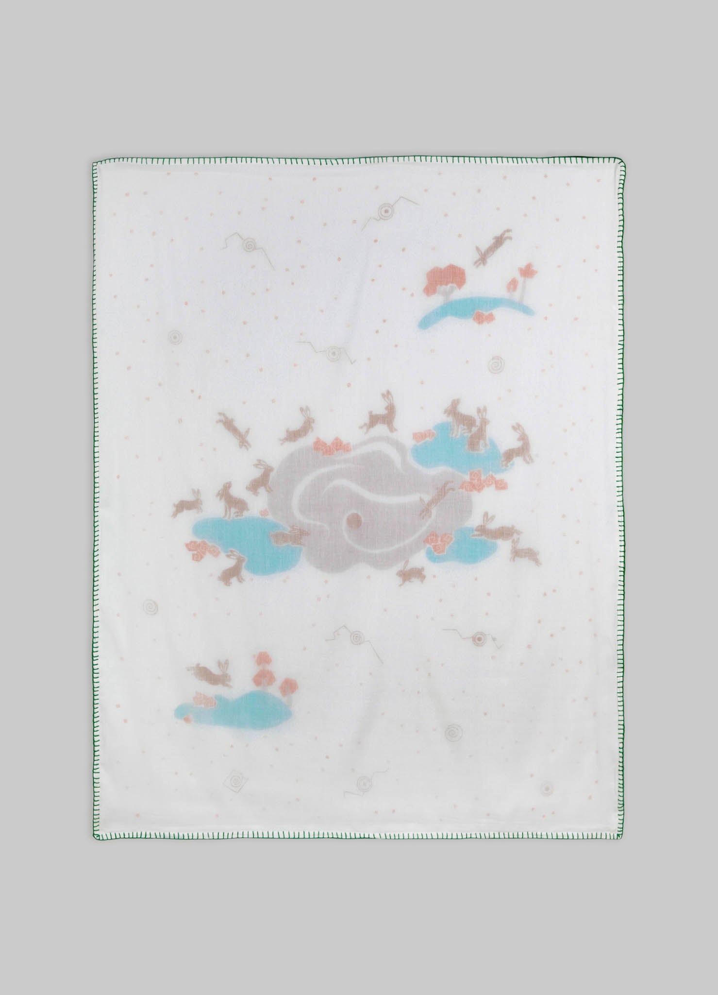 Baby burp cloth made of soft white fabric with printed pastel illustrations of rabbits, clouds, and flying birds, edged with green stitching.