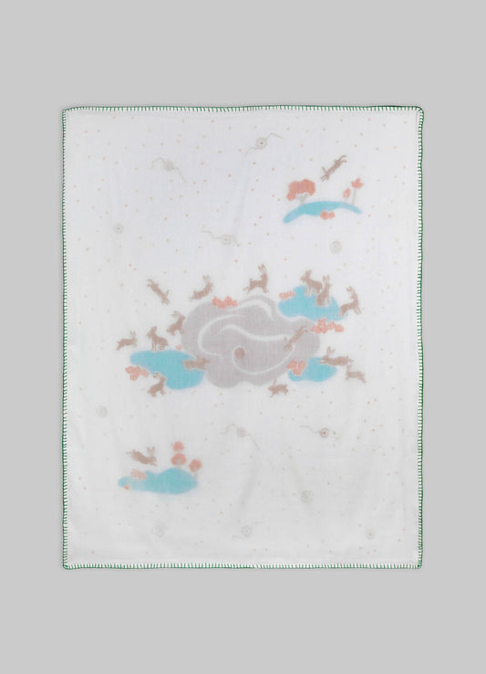 Baby burp cloth made of soft white fabric with printed pastel illustrations of rabbits, clouds, and flying birds, edged with green stitching.