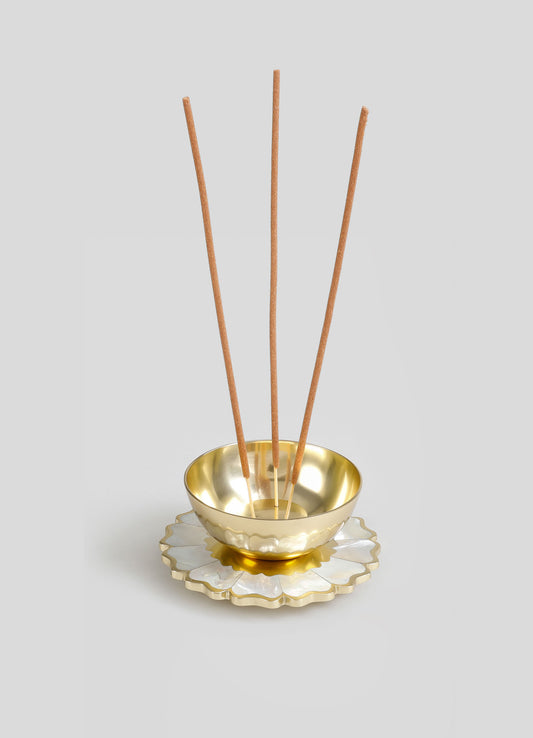 A decorative incense holder featuring a scalloped ceramic tray with a glossy white and gold finish, holding a smaller gold-toned bowl with a smooth, reflective surface. Four thin, elongated incense sticks are arranged in the bowl against a plain, light gray background.