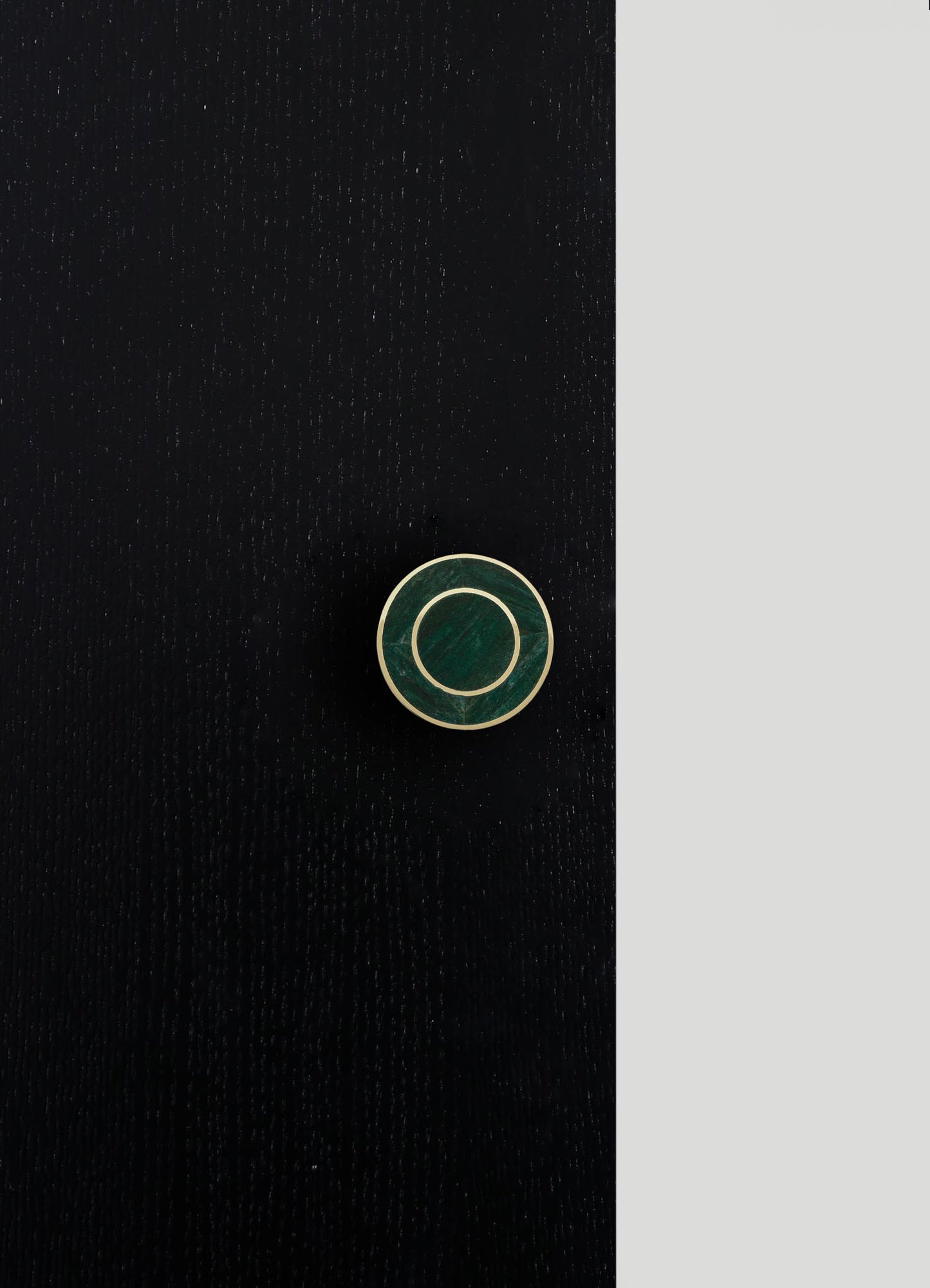 A round jewelry box with a dark green marble lid and gold accents, set against a black and gray background.