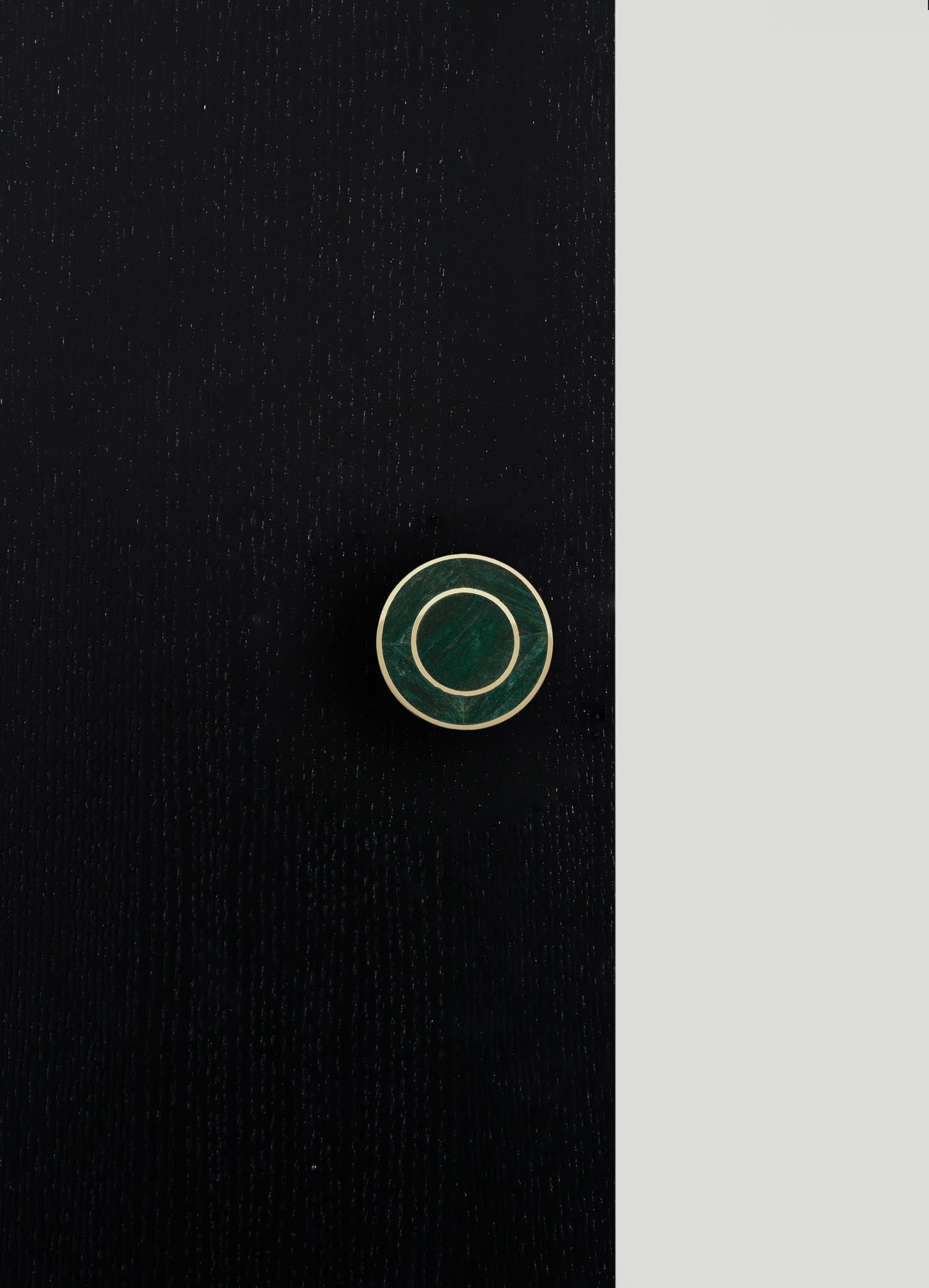 A round jewelry box with a dark green marble lid and gold accents, set against a black and gray background.