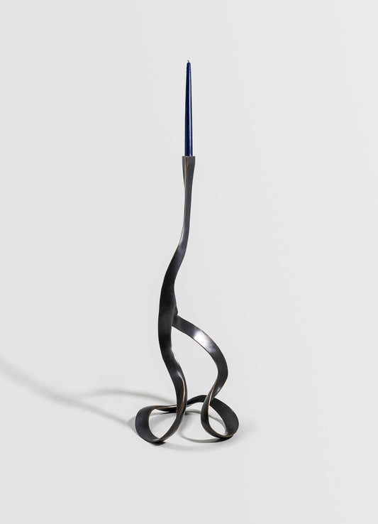 A wrought iron candlestick holder with a sculptural, twisted design in a matte black finish, holding a slim, dark blue taper candle.