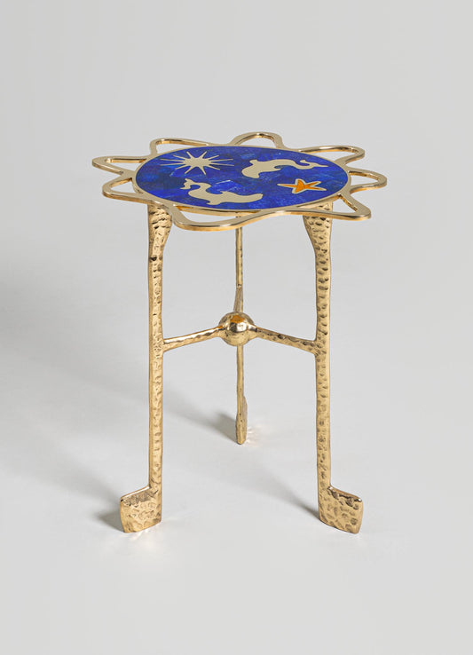 A small side table with a gold-finished hammered metal frame and three legs, featuring a round top with a blue and gold celestial motif pattern.