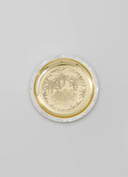 A decorative round tray made of metal with a gold finish, featuring an engraved tropical scene with palm trees and animals, bordered by a translucent, iridescent rim.
