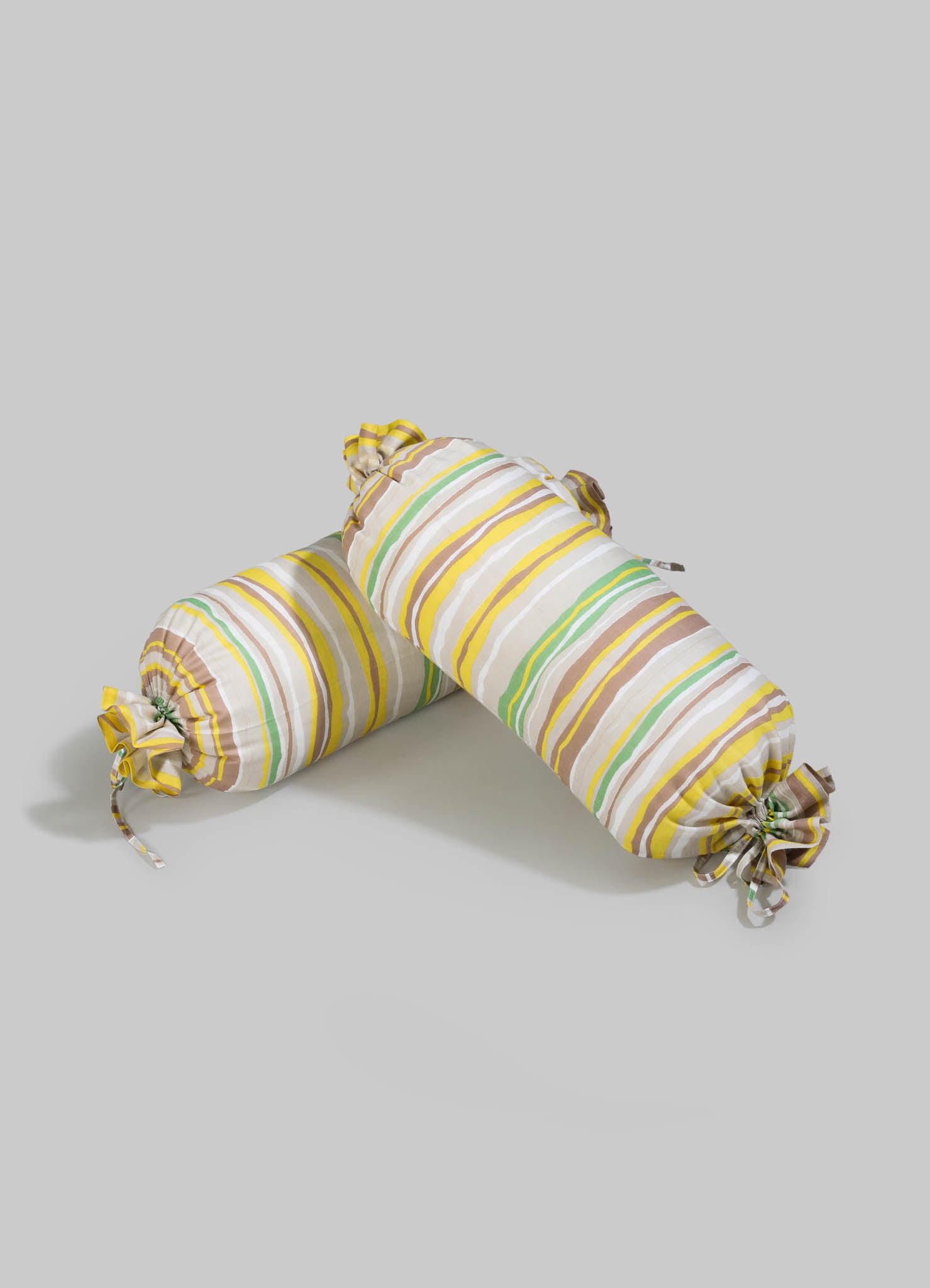 Striped fabric bolster cushions with pastel yellow, green, brown, and white tones, featuring ruffled ends with tied bows, designed for decorative or comfort use.