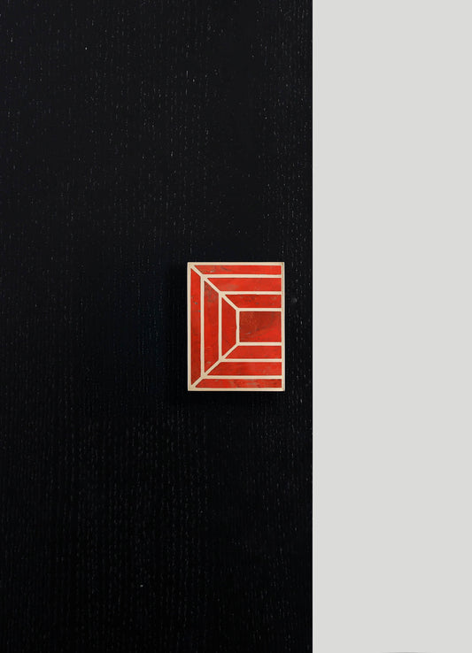 A rectangular ceramic box with a red and white geometric pattern featuring lines that form a three-dimensional cube effect, placed on a black textured surface with a light gray background.