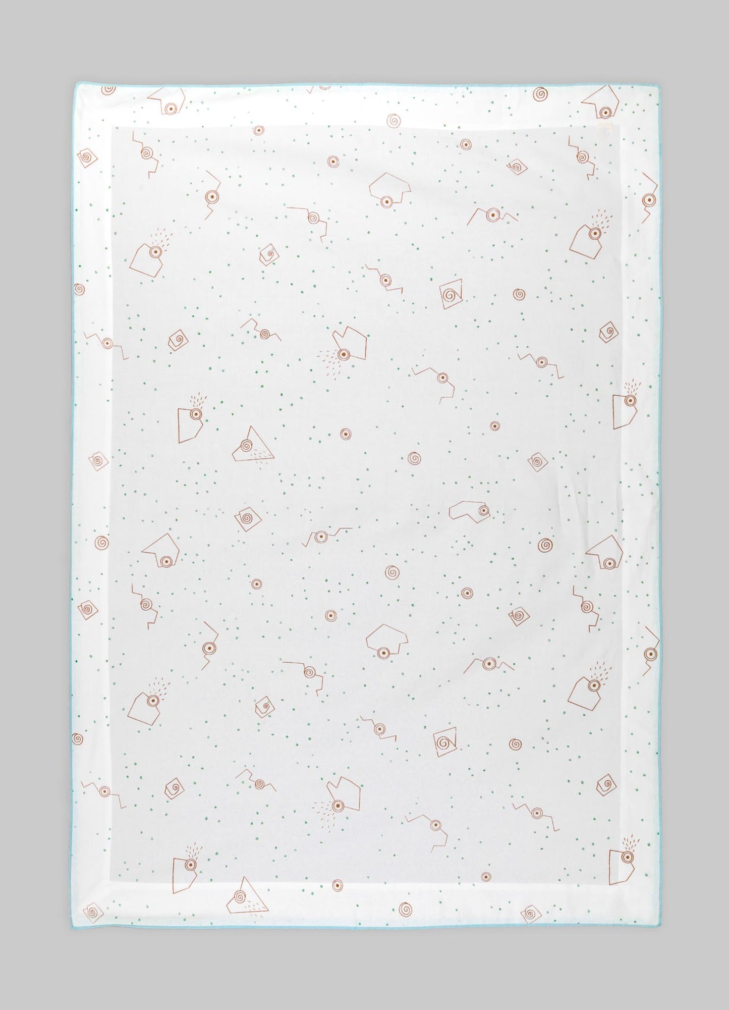 A transparent tablecloth with a printed pattern of orange geometric shapes, small green dots, and abstract motifs, laid flat on a gray surface.
