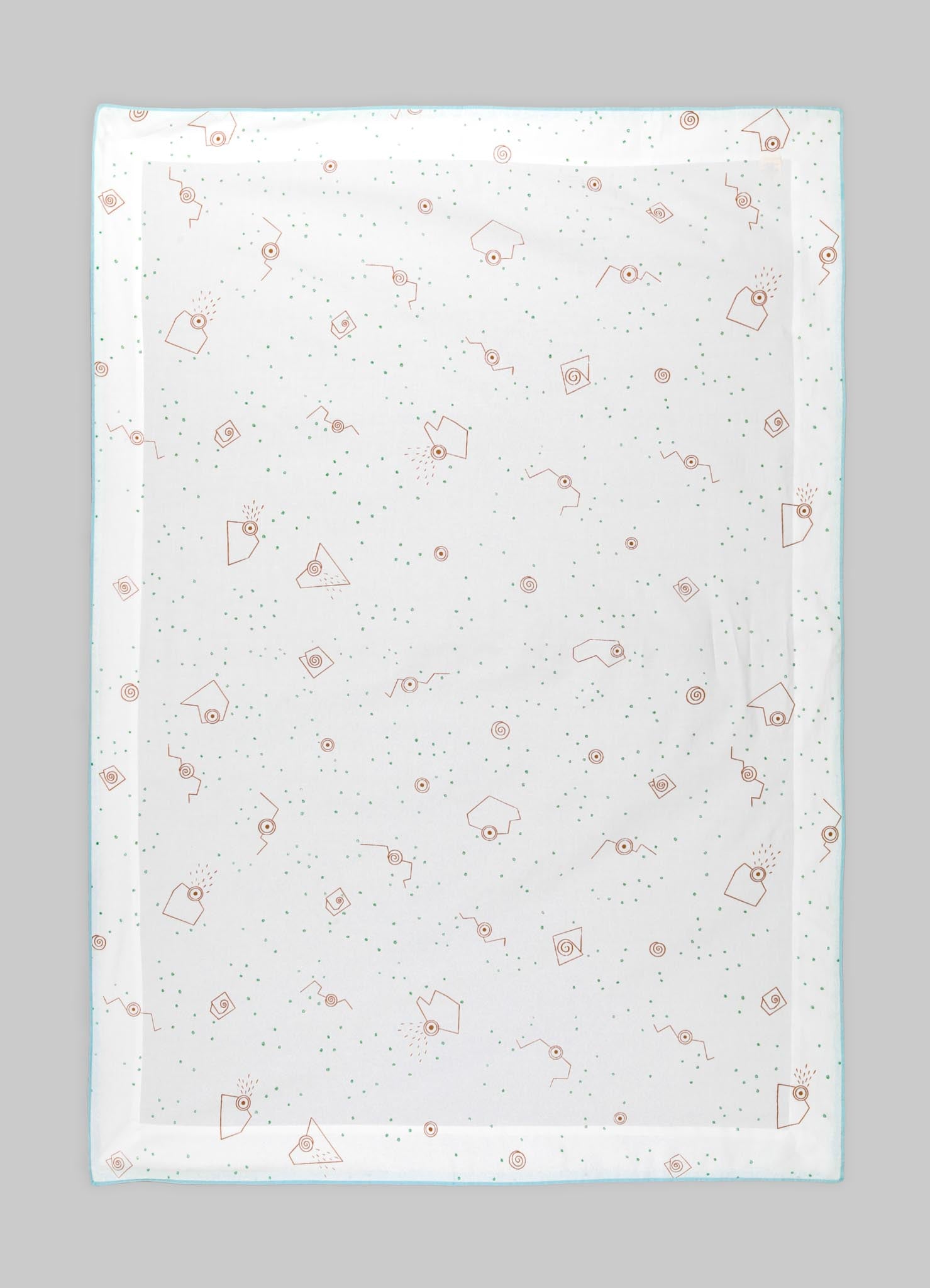 A transparent tablecloth with a printed pattern of orange geometric shapes, small green dots, and abstract motifs, laid flat on a gray surface.