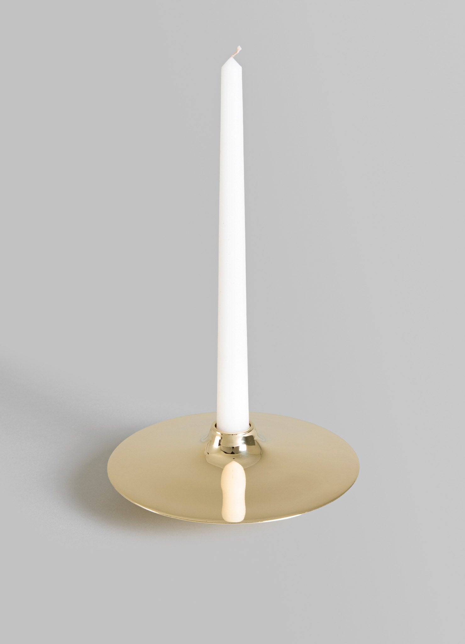 A modern brass candle holder with a round, flat base and a white pillar candle. The design features a sleek, contemporary style with a polished metallic finish.