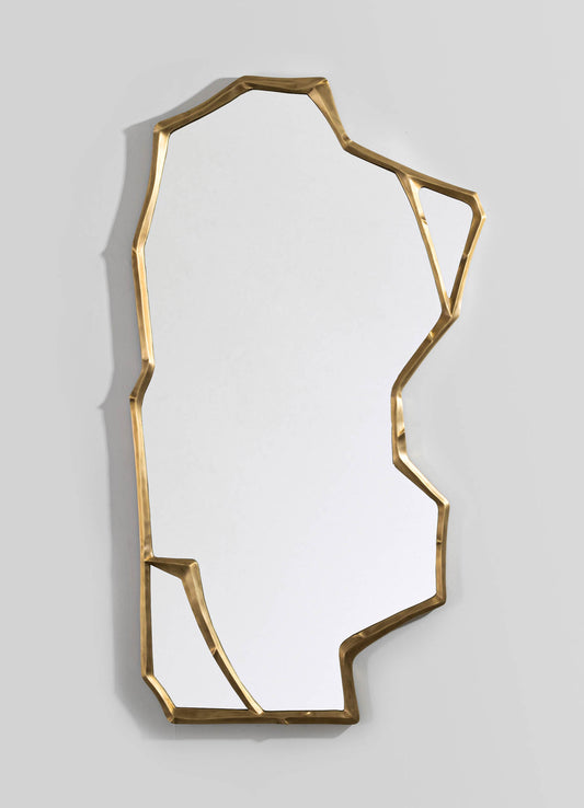 Decorative wall mirror with an irregular, geometric brass frame and a plain reflective surface, mounted on a light gray wall.