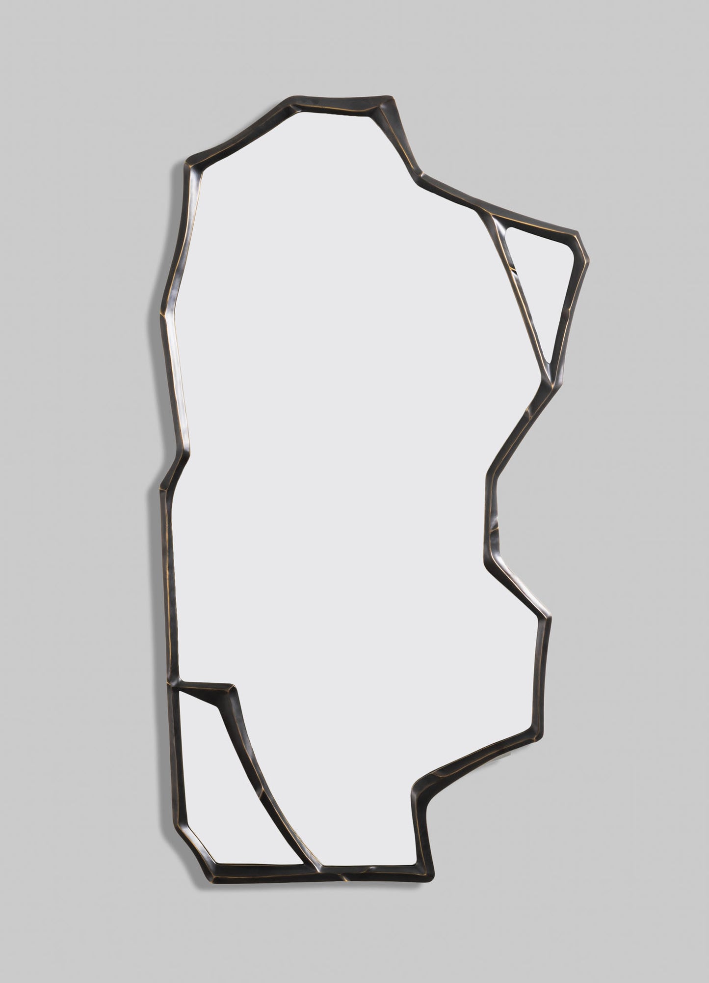 A decorative wall mirror with an irregular, geometric metal frame in dark bronze or black finish, set against a light-colored wall. The mirror has an abstract, contemporary style with angular lines and a minimalist appearance.