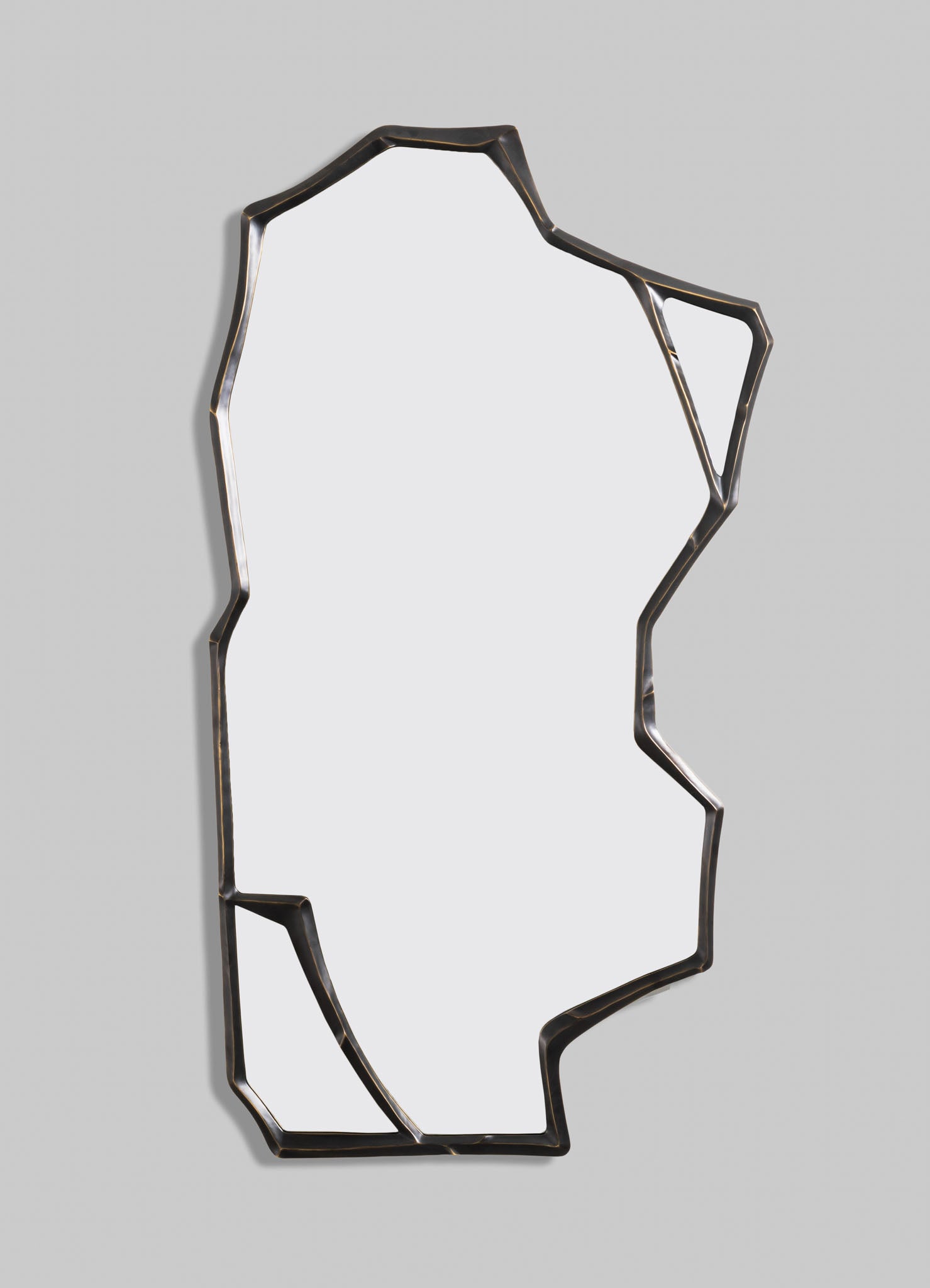 A decorative wall mirror with an irregular, geometric metal frame in dark bronze or black finish, set against a light-colored wall. The mirror has an abstract, contemporary style with angular lines and a minimalist appearance.