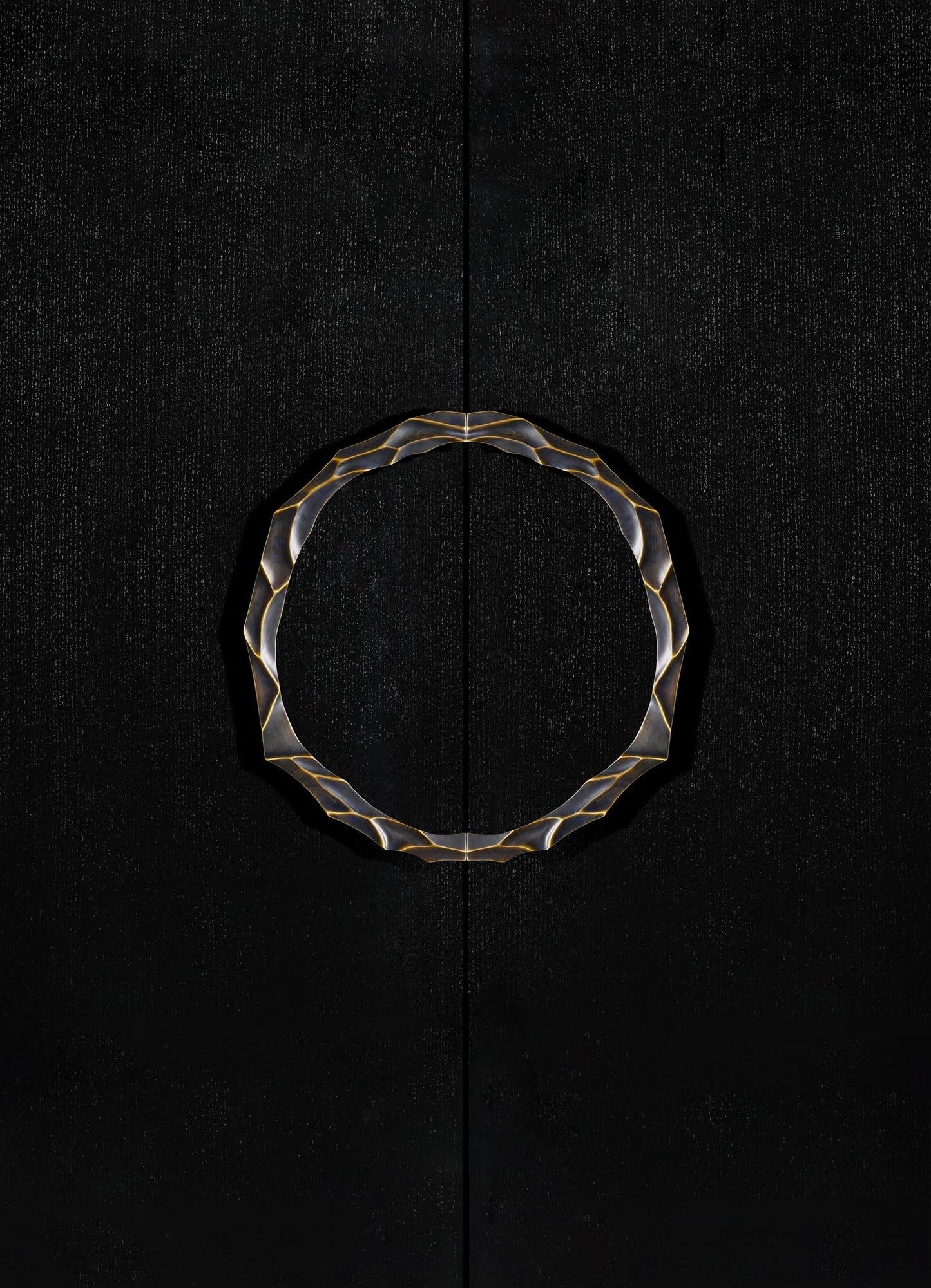 A circular decorative mirror with a wavy, metallic gold frame mounted on a black textured wall. The mirror's design has an abstract, contemporary style.