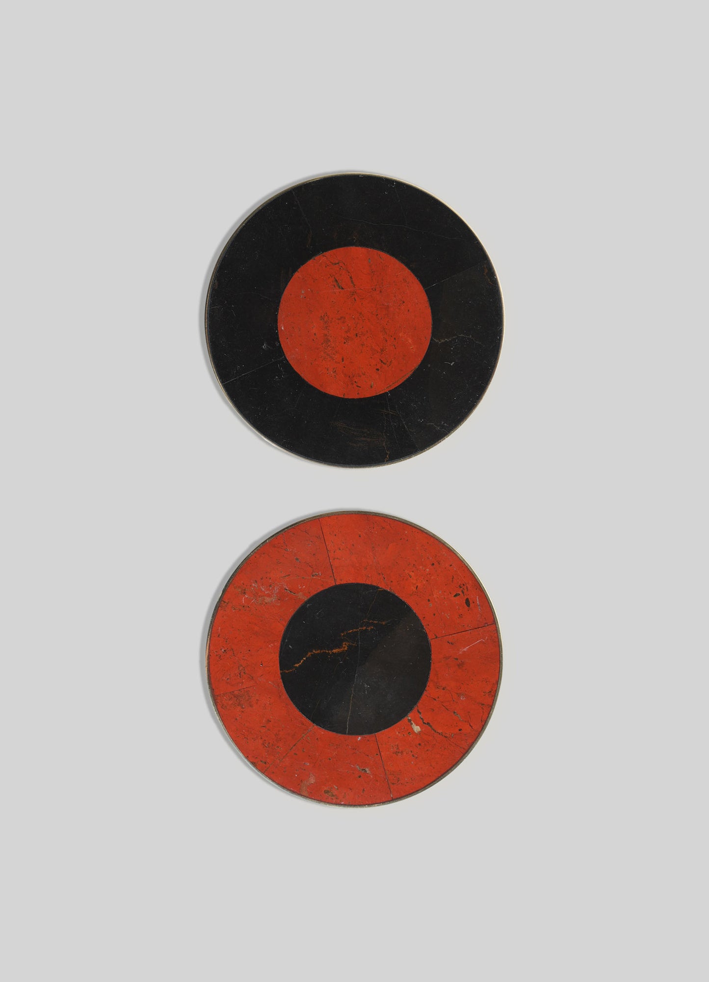 Two circular wall plates with a bold geometric design featuring black and red-orange coloration, resembling abstract eye motifs. The plates have a vintage, distressed finish with visible scratches and crack lines.