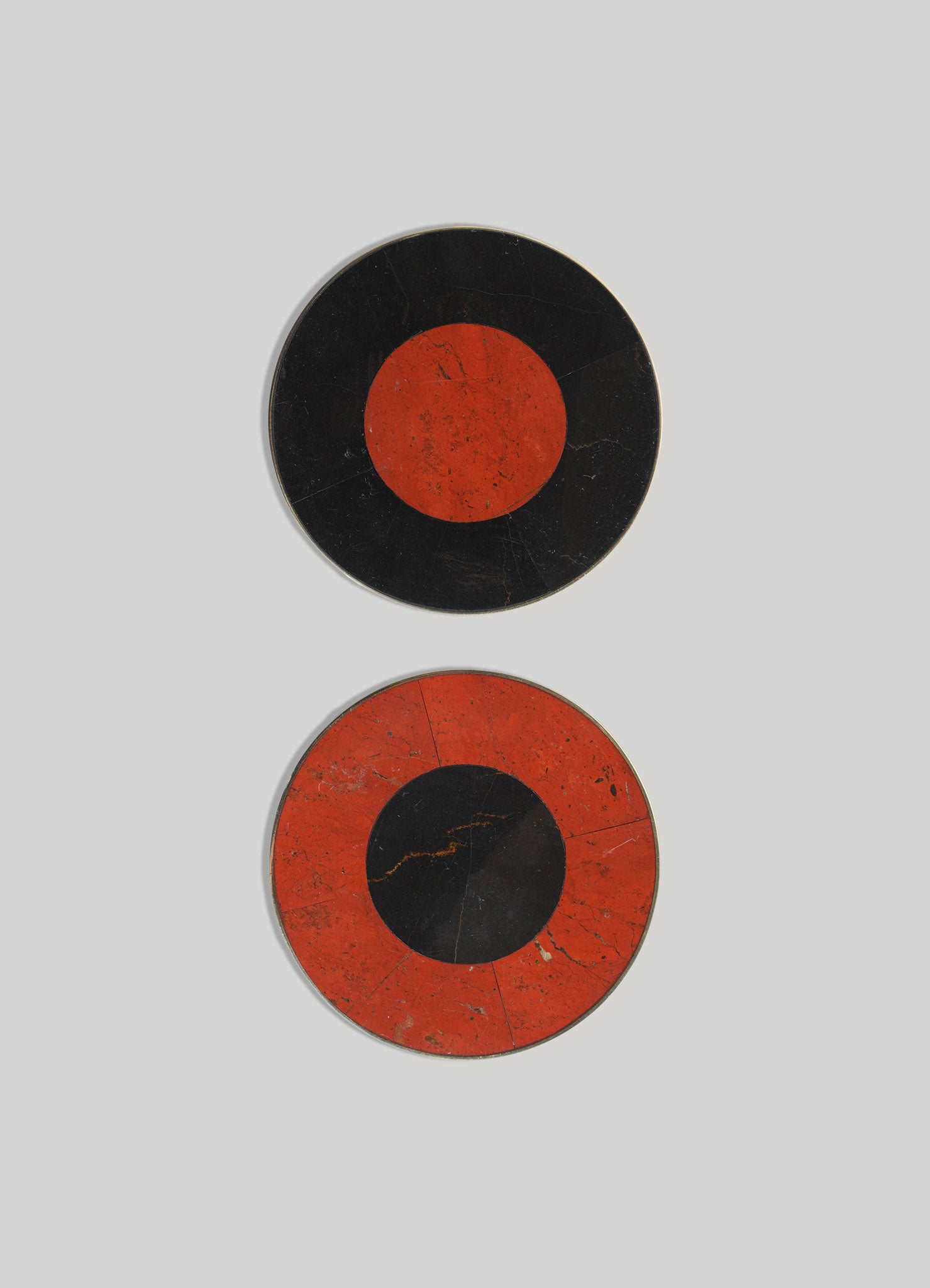 Two circular wall plates with a bold geometric design featuring black and red-orange coloration, resembling abstract eye motifs. The plates have a vintage, distressed finish with visible scratches and crack lines.
