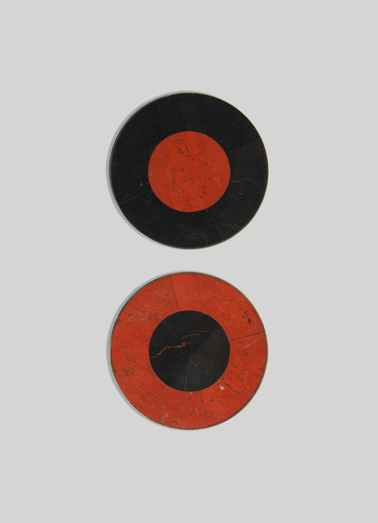 Two circular wall plates with a bold geometric design featuring black and red-orange coloration, resembling abstract eye motifs. The plates have a vintage, distressed finish with visible scratches and crack lines.