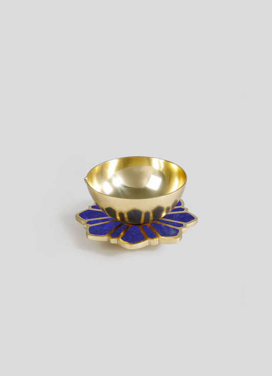 A decorative bowl with a shiny gold interior and exterior, placed on a blue and gold floral-shaped base.