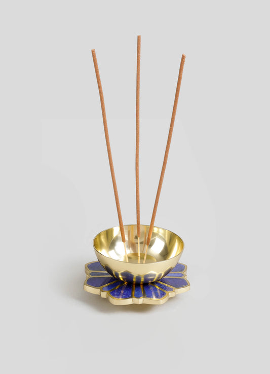 A decorative incense holder with a metallic gold bowl resting on a ceramic base featuring a blue and gold floral pattern. Four thin wooden sticks are inserted into the bowl, designed for holding incense.