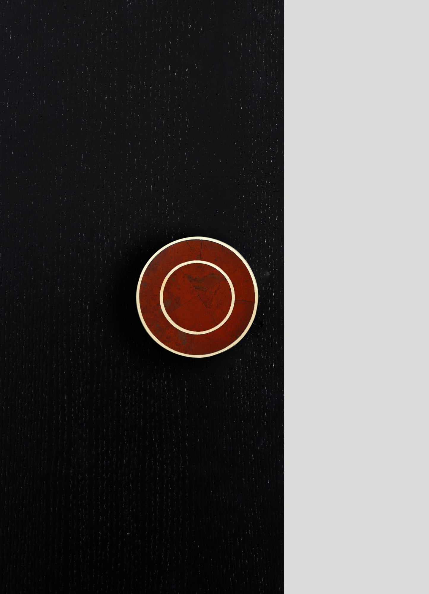 A round, tabletop ceramic dish with a deep red, marbled finish and contrasting white rim, set against a black textured surface. The dish features a geometric design with concentric circles and subtle cracks, conveying a contemporary, artisanal style.