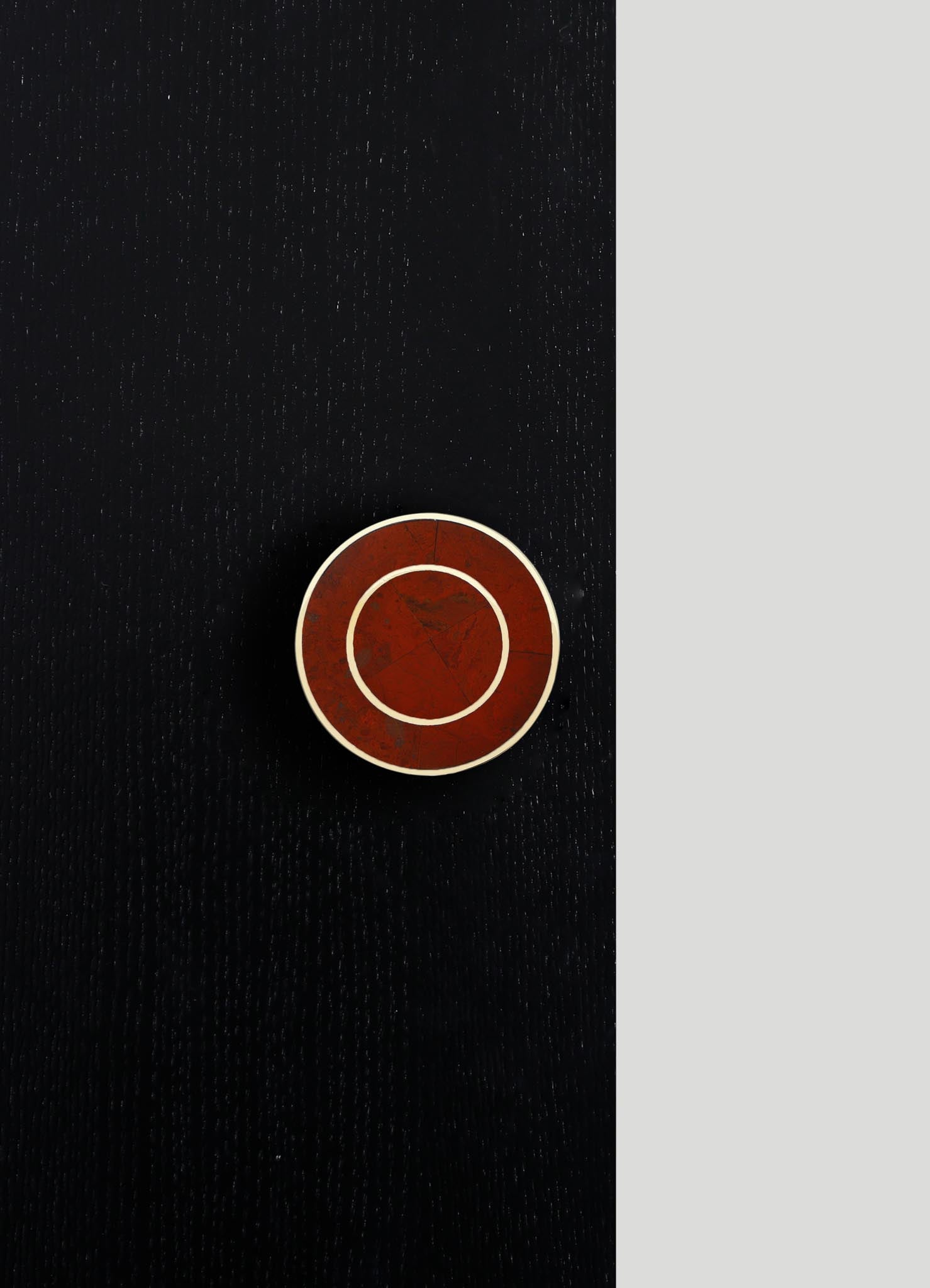 A round, tabletop ceramic dish with a deep red, marbled finish and contrasting white rim, set against a black textured surface. The dish features a geometric design with concentric circles and subtle cracks, conveying a contemporary, artisanal style.