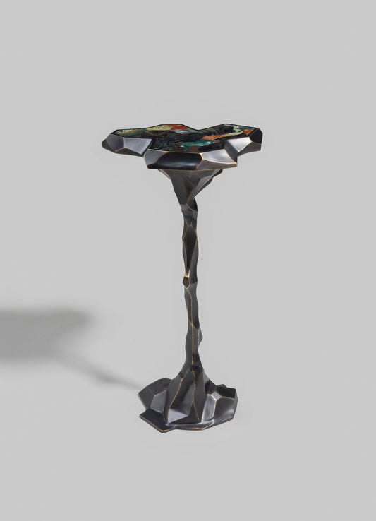 A sculptural side table with a mosaic stone top featuring a mix of colorful, patterned tiles and a sculpted, metallic-finish base with an organic, irregular shape.