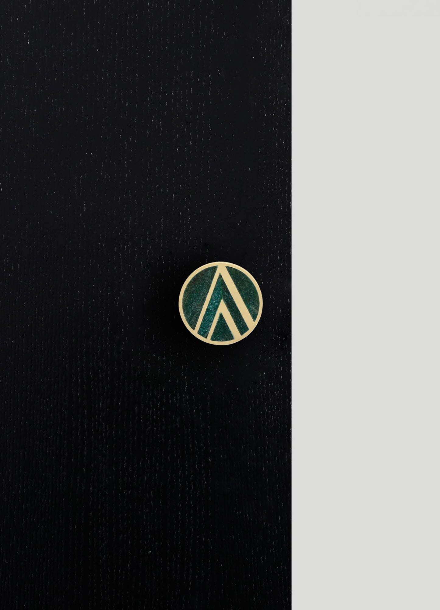 A round enamel pin featuring a geometric pattern of green and white lines on a black background, with a contrasting gray border.