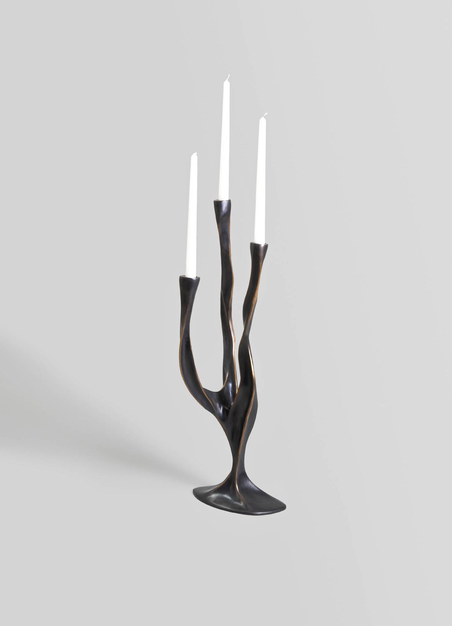 Brass candle holder with an organic, twisting design and a dark, antique finish, holding three white taper candles.
