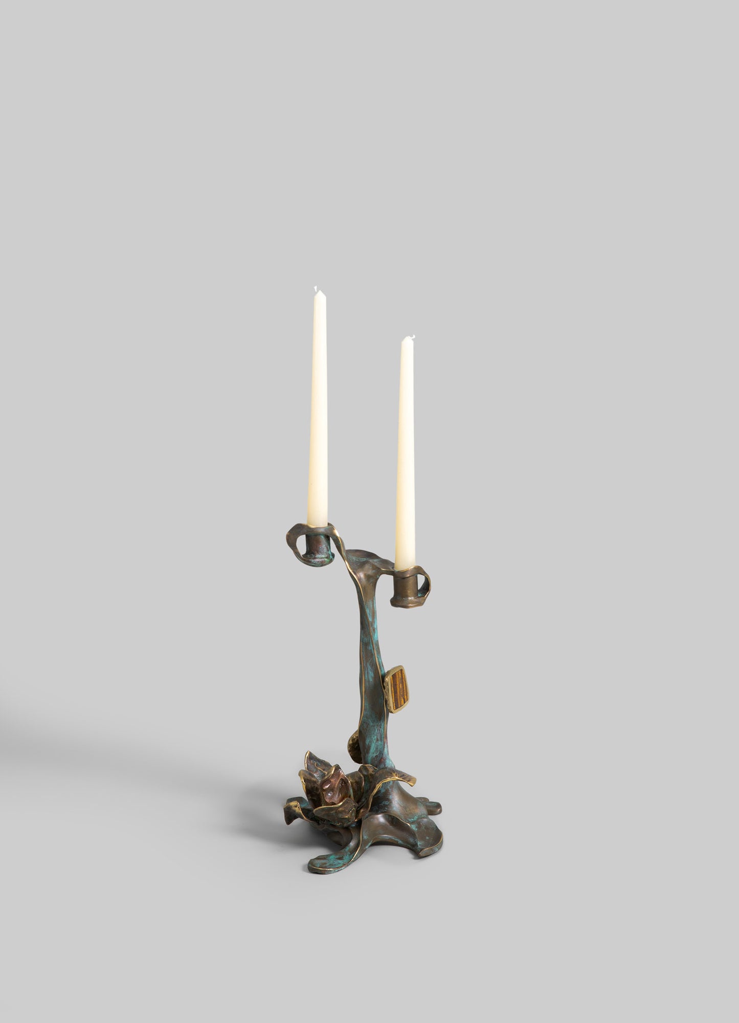 Brass candelabrum with an organic, sculptural design supporting two tall white taper candles, featuring a distressed patina finish.