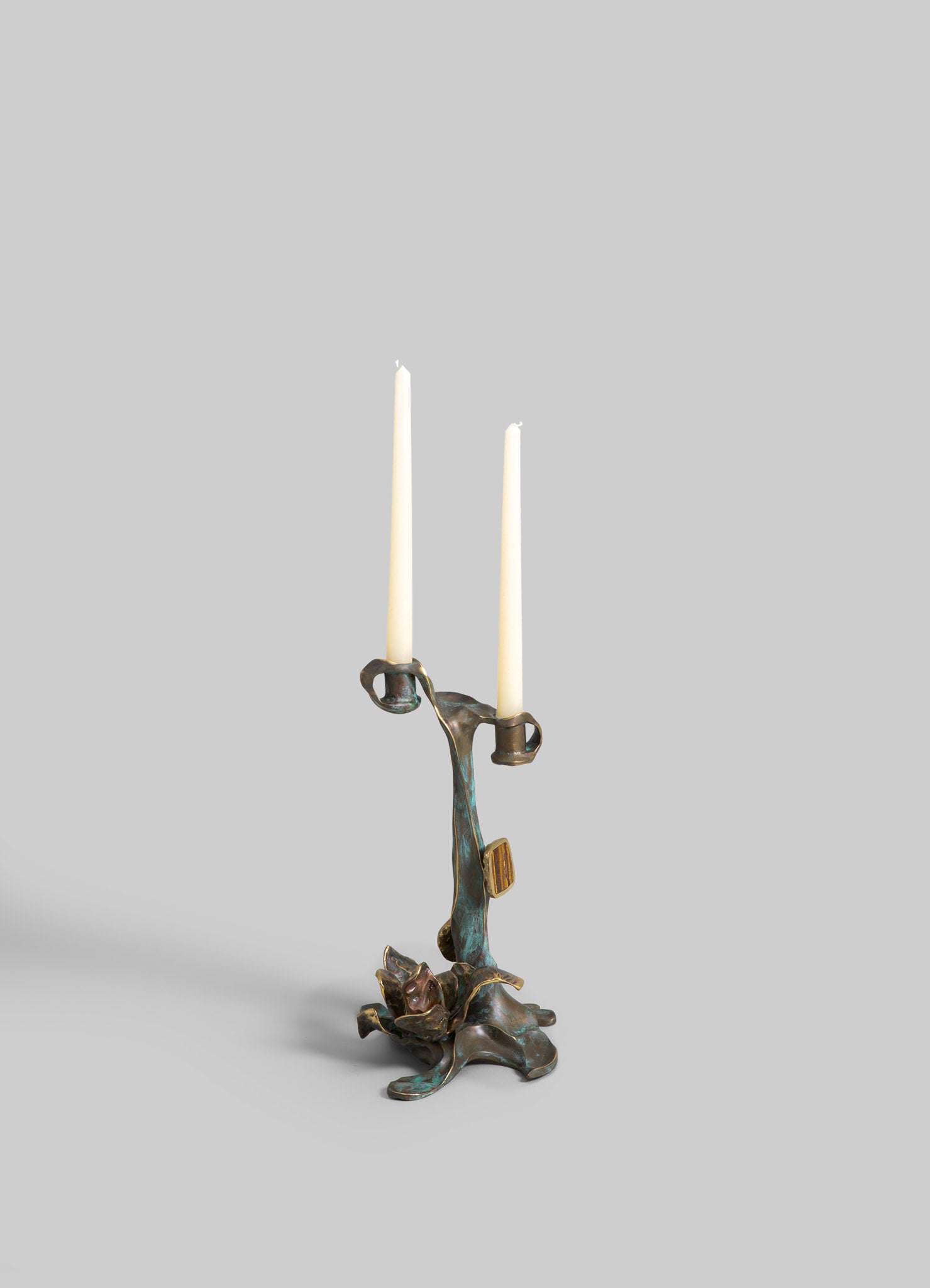 Brass candelabrum with an organic, sculptural design supporting two tall white taper candles, featuring a distressed patina finish.