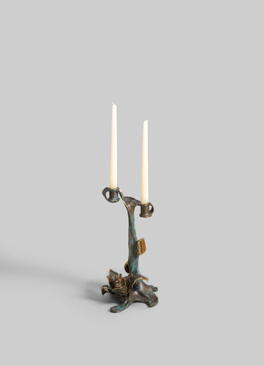 Brass candelabrum with an organic, sculptural design supporting two tall white taper candles, featuring a distressed patina finish.