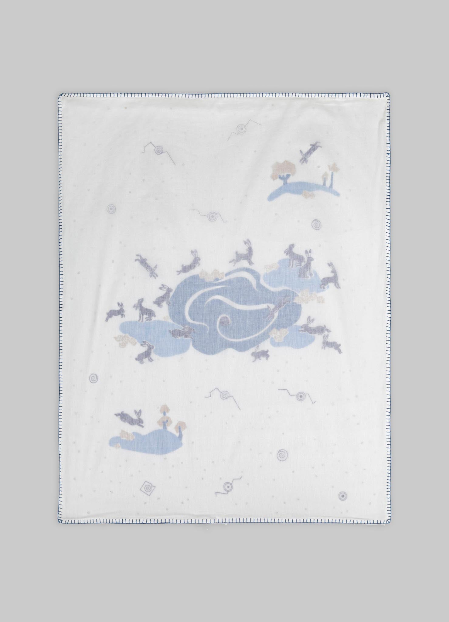 Cotton tablecloth with a whimsical animal and cloud pattern in soft pastel blue and beige tones, featuring embroidered border detail.