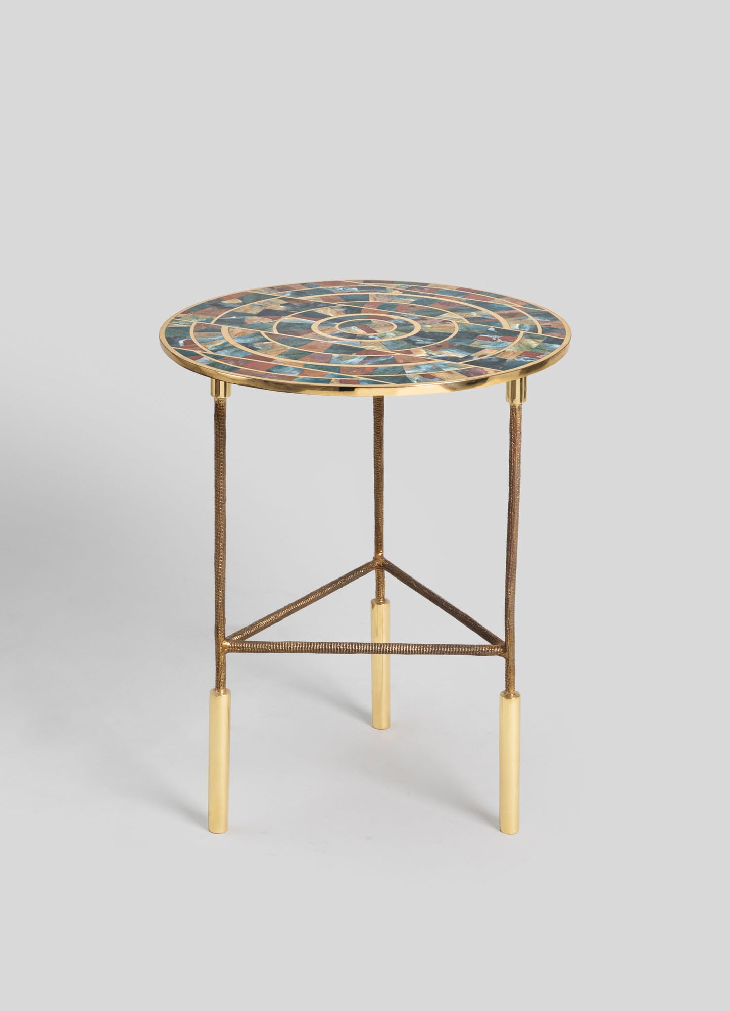 A round side table with a mosaic top featuring multicolored stone tiles arranged in a spiral pattern. The table has a metal base with a gold finish, slender legs, and a triangular support structure.