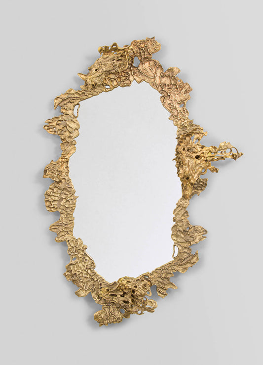 A decorative mirror with an ornate gold-colored frame featuring an irregular, textured pattern resembling abstract organic shapes, mounted on a plain, light-colored wall.